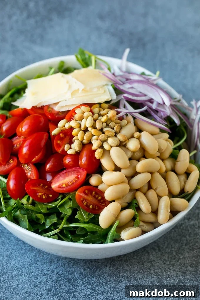 Arugula Salad Recipe | Green Salad | White Bean Salad #salad #arugula #cleaneating #lowcarb #keto #dinneratthezoo A bowl filled with fresh arugula, cherry tomatoes, pine nuts, thinly sliced red onion, and shaved Parmesan cheese, awaiting its dressing.