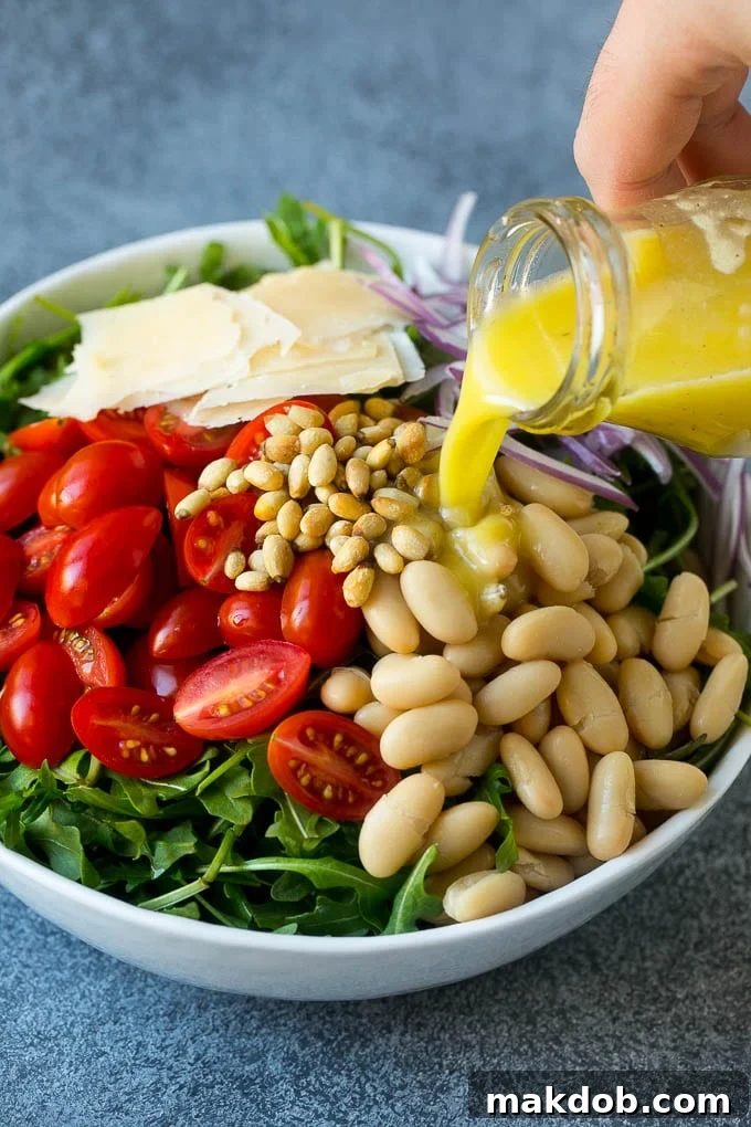 Arugula Salad Recipe | Green Salad | White Bean Salad #salad #arugula #cleaneating #lowcarb #keto #dinneratthezoo White beans, cherry tomatoes, pine nuts, shaved Parmesan, and red onion in a bowl, with lemon dressing being poured over for tossing.
