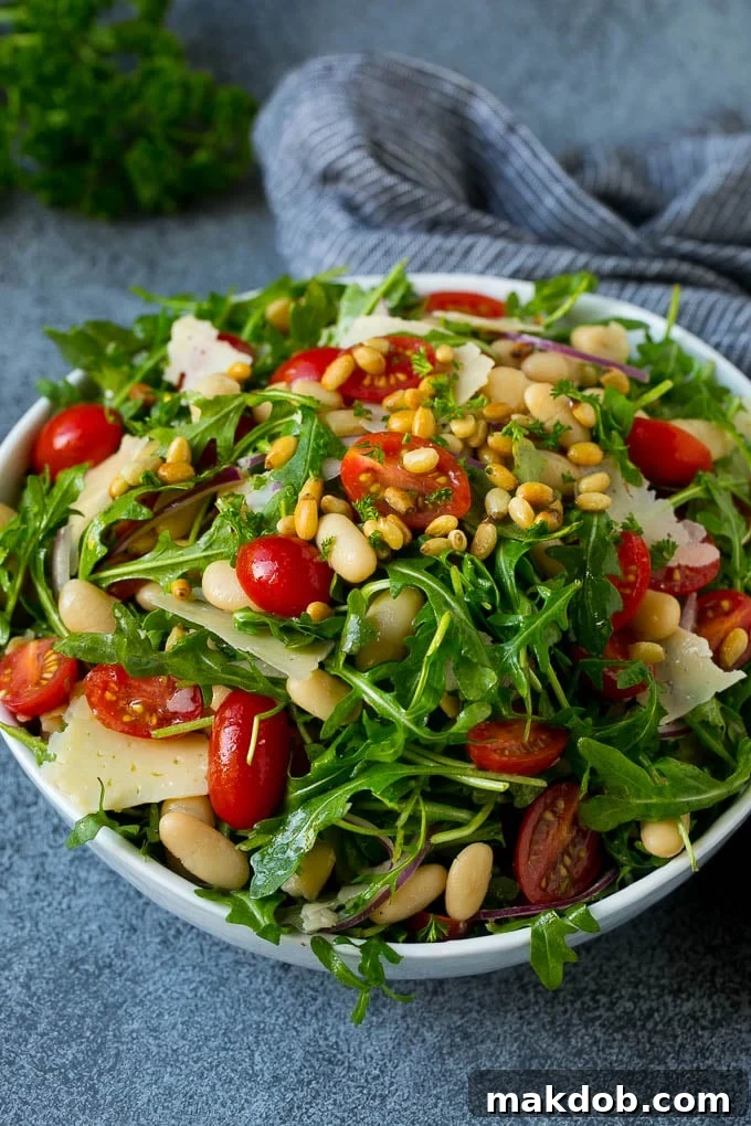 Arugula Salad Recipe | Green Salad | White Bean Salad #salad #arugula #cleaneating #lowcarb #keto #dinneratthezoo A close-up of a bowl of arugula salad, showcasing cherry tomatoes, pine nuts, red onion, and shaved cheese amidst the fresh greens.