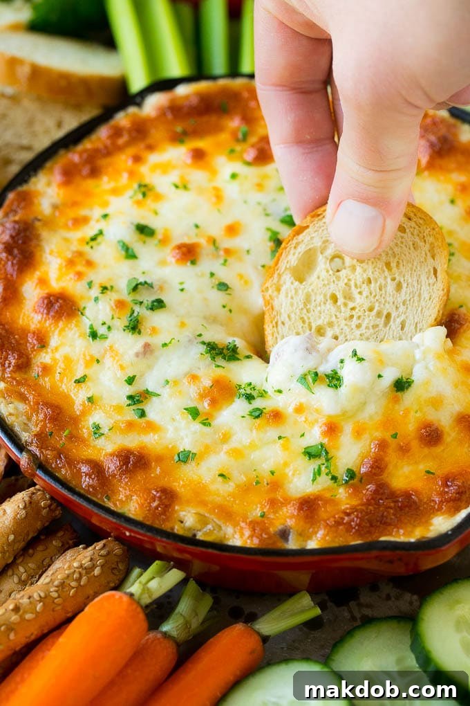 A hand scooping out a serving of hot, cheesy Reuben dip with a baguette slice, showing its creamy texture and visible pieces of corned beef and sauerkraut.