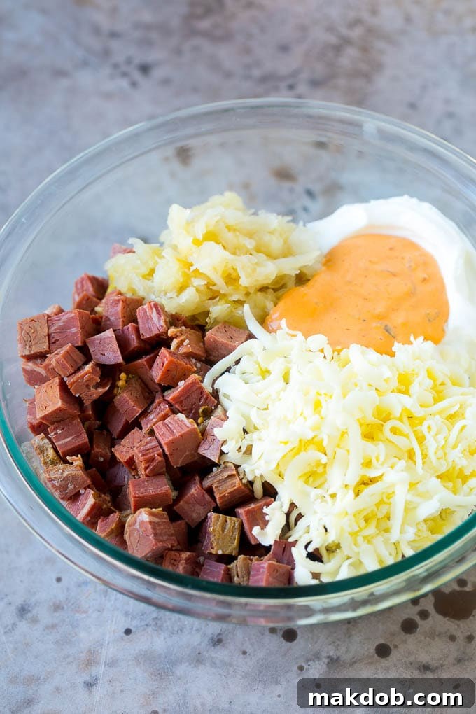 A bowl filled with the key ingredients for Reuben dip: corned beef, softened cream cheese, Thousand Island dressing, and shredded Swiss cheese, ready to be mixed.