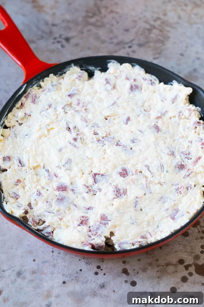 Cream cheese, corned beef, and other ingredients for Reuben dip spread evenly into an oven-safe skillet, ready for baking.