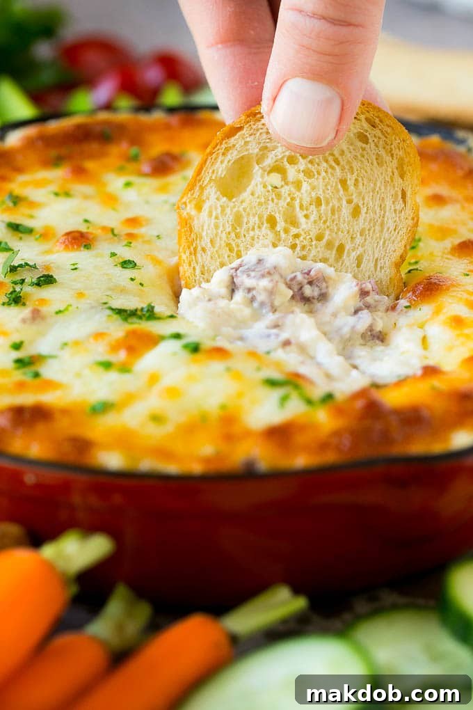 A crisp baguette chip being dipped into a skillet of hot, bubbly Reuben dip, highlighting its rich, cheesy texture and inviting warmth.