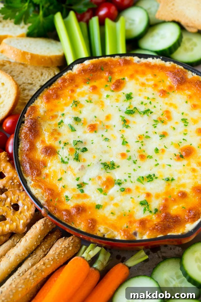 A baked skillet of Reuben dip, golden and bubbly, served beautifully on a platter with an assortment of dippers including crackers, celery sticks, and other vegetables.