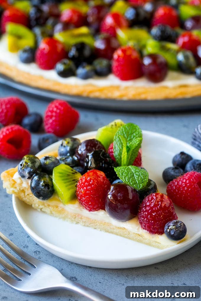 Serving a Slice of Fruit Pizza A single slice of fruit pizza topped with cream cheese frosting and mixed berries, on a white plate.