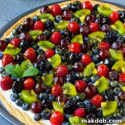 Fruit pizza with a sugar cookie crust and cream cheese frosting, topped with berries, kiwi and grapes.