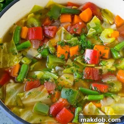 A pot of cabbage soup with carrots, celery, bell peppers and green beans.