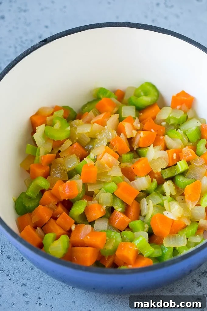 Freshly chopped carrots, onions, and celery sautéing in a large soup pot, forming the aromatic base for cabbage soup.