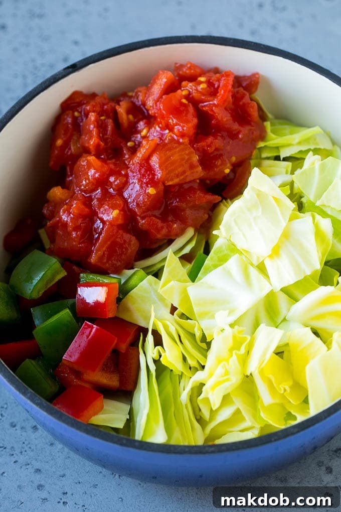 Vibrant red and green bell peppers, diced tomatoes, and other raw vegetables added to a large pot, ready to simmer into a delicious cabbage soup.