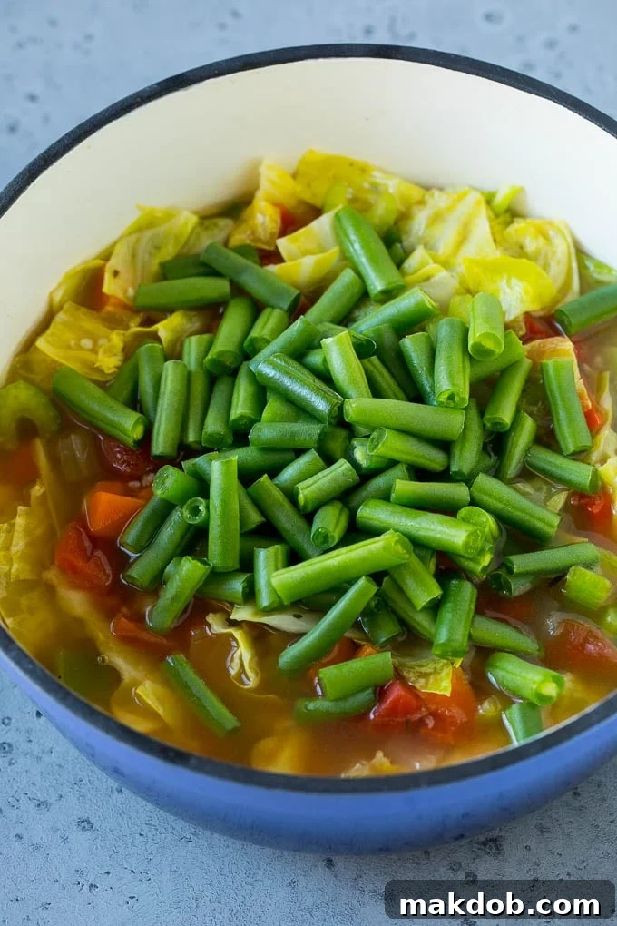 Fresh green beans added to a pot of simmering, cooked vegetables, enhancing the texture and nutrition of the cabbage soup.