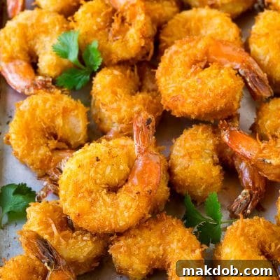A pile of crispy coconut shrimp on a sheet pan with cilantro leaves for garnish.