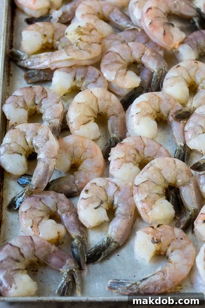 Large raw tail-on shrimp arranged on a sheet pan, ready for preparation.