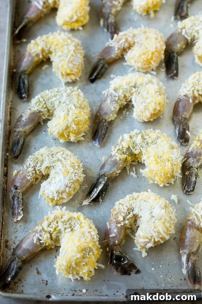 Raw shrimp coated with breadcrumbs and shredded coconut, laid out on a baking sheet before cooking.