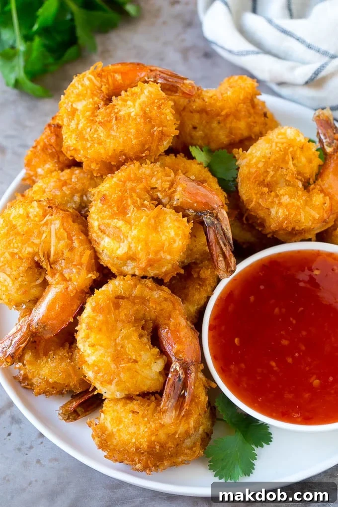 A plate of golden crispy coconut shrimp served with a small bowl of sweet chili sauce, garnished with fresh herbs.