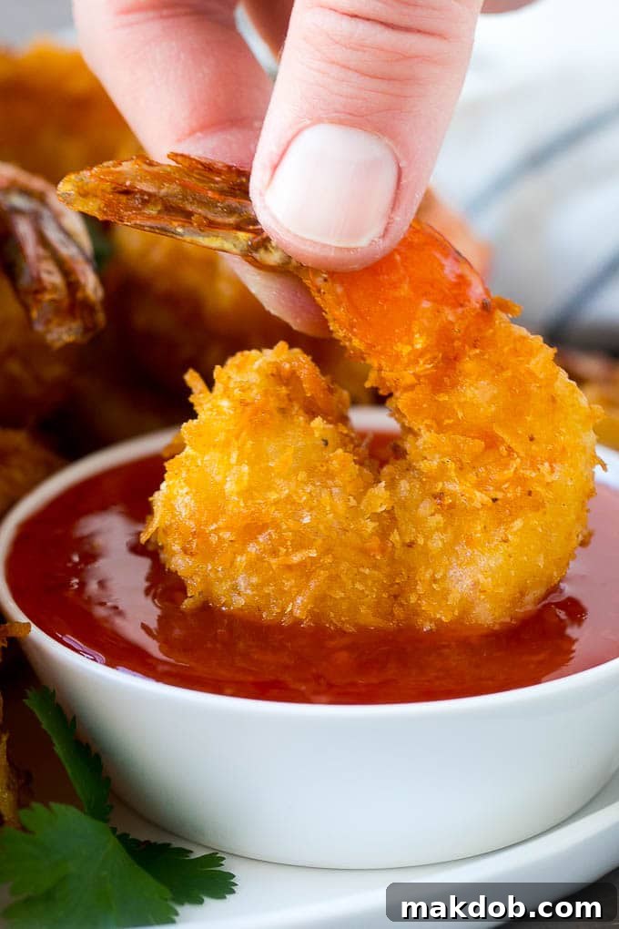 A hand dipping a crispy prawn into a bowl of sweet chili sauce, highlighting the crunchy texture.