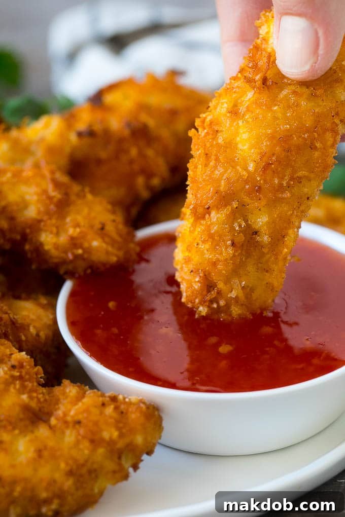 A hand dipping coconut chicken into sweet chili sauce.