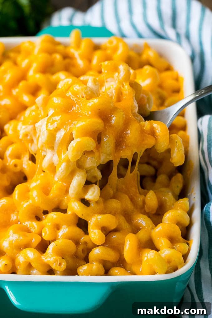 A generous serving of creamy baked mac and cheese. Baked mac and cheese with a serving spoon lifting up a portion, showcasing its creamy texture.