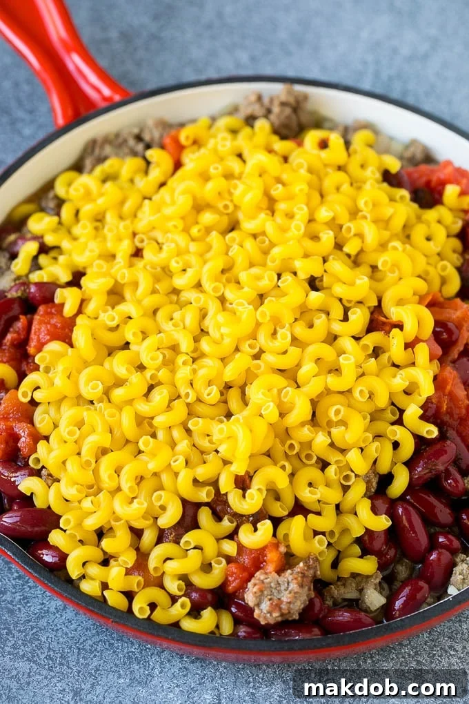Uncooked macaroni in a skillet with ground beef and tomatoes.