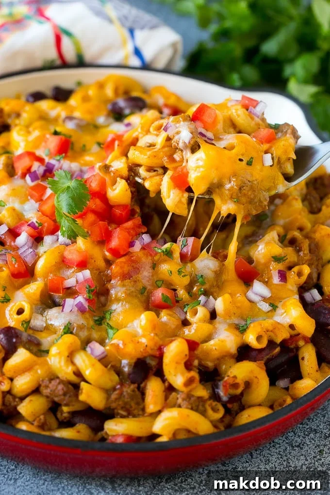 A serving spoon in a pan of chili mac scooping up a portion.
