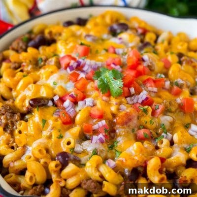 A skillet of chili mac topped with melted cheese, diced tomatoes and minced onion.