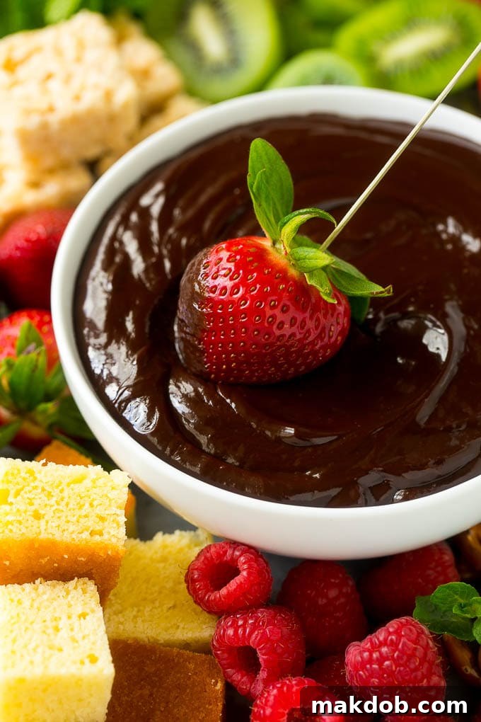 A strawberry being dipped into a bowl of rich chocolate fondue.