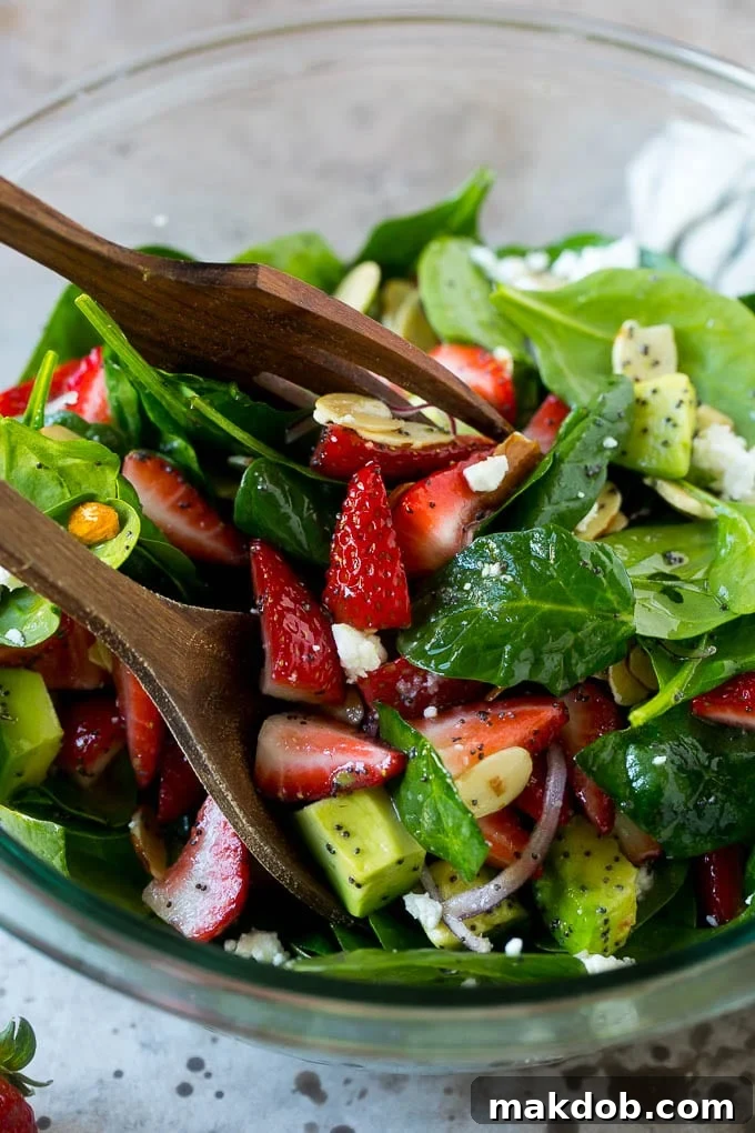 Salad tongs in a bowl of spinach salad with strawberries.