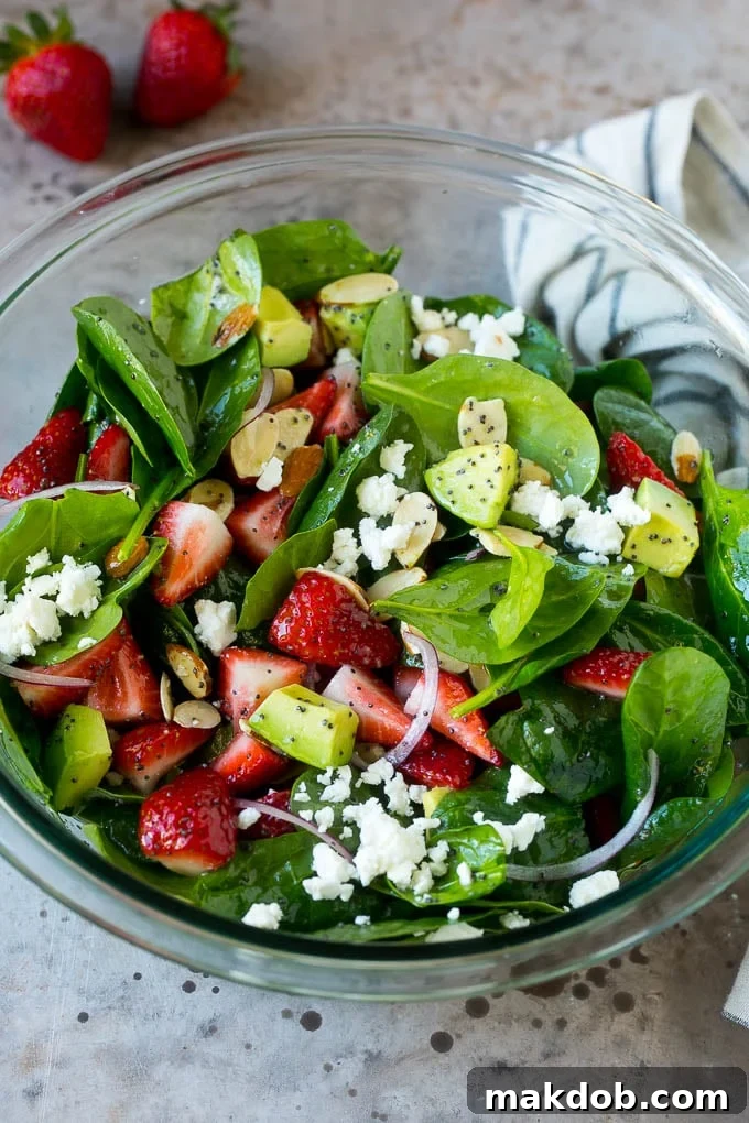 A bowl of strawberry spinach salad with feta cheese, almonds and avocado.