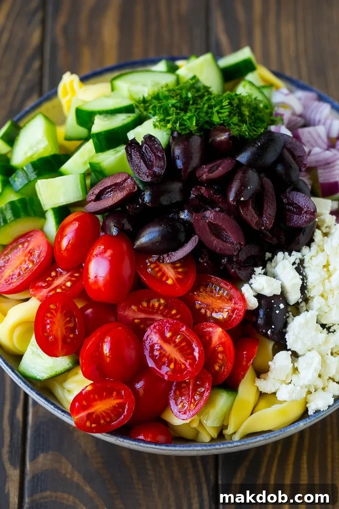 A large bowl of Greek Tortellini Salad, generously topped with an assortment of olives, cherry tomatoes, crisp cucumber, and creamy feta cheese, highlighting its vibrant ingredients.