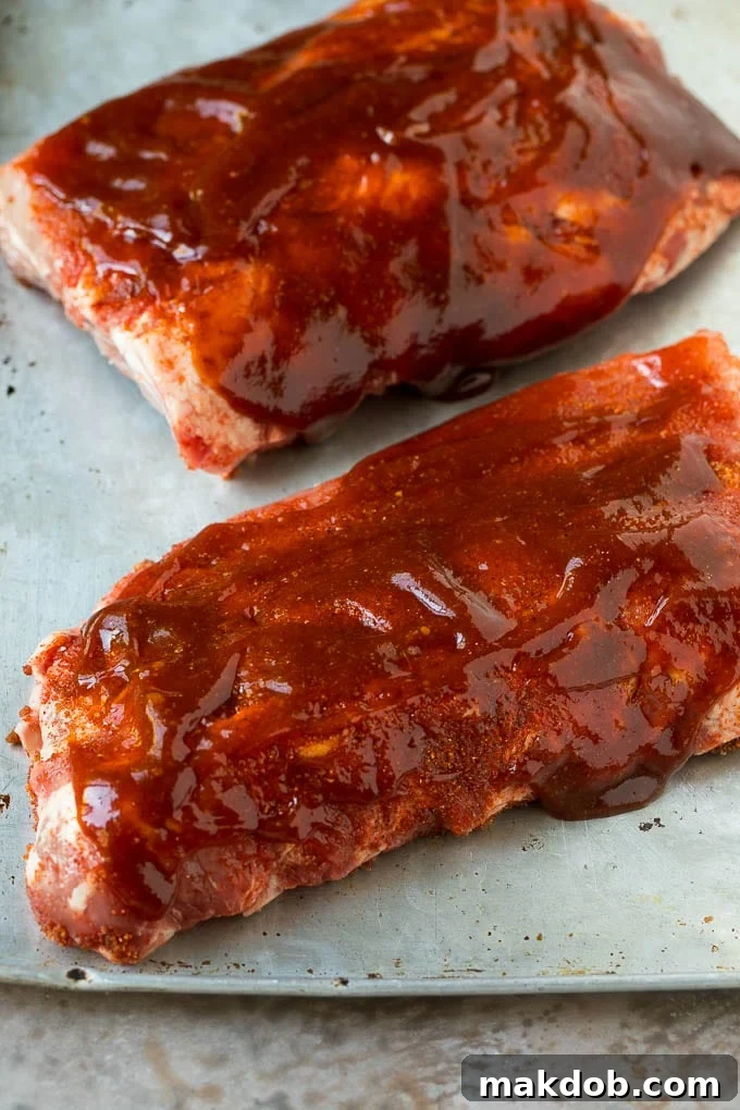 Two slabs of raw baby back ribs, already coated in barbecue sauce, ready for cooking.