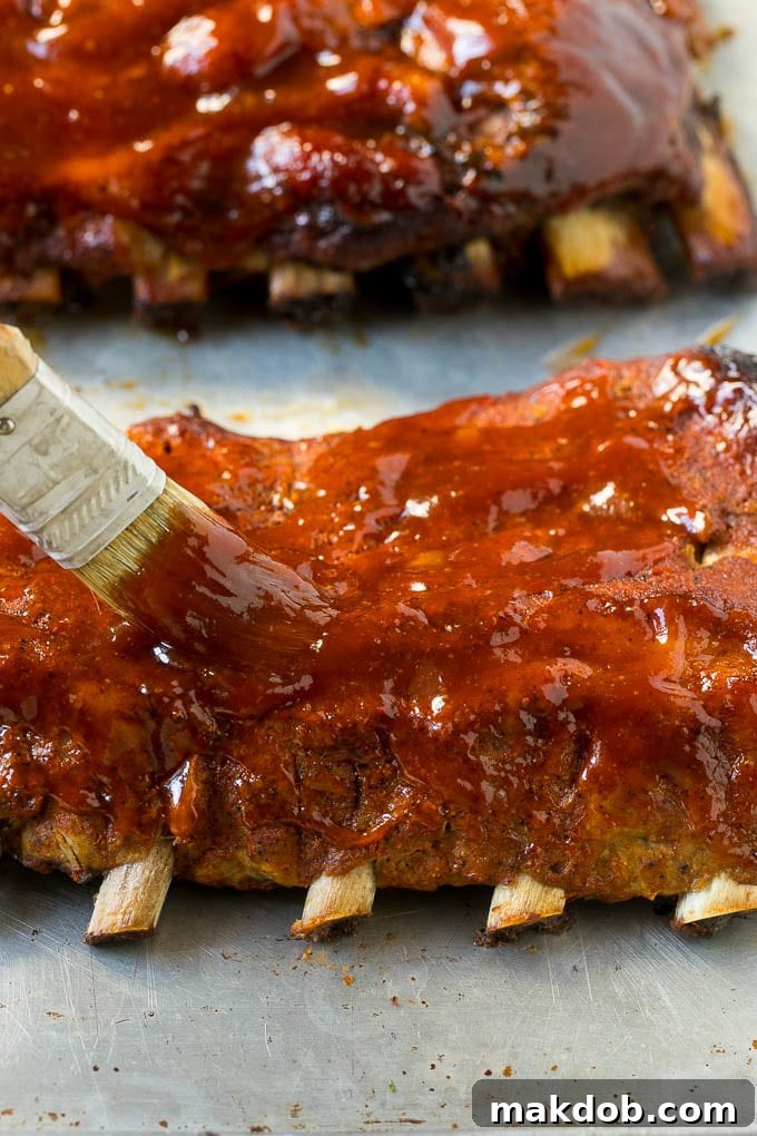 A brush coating cooked pork ribs with BBQ sauce.