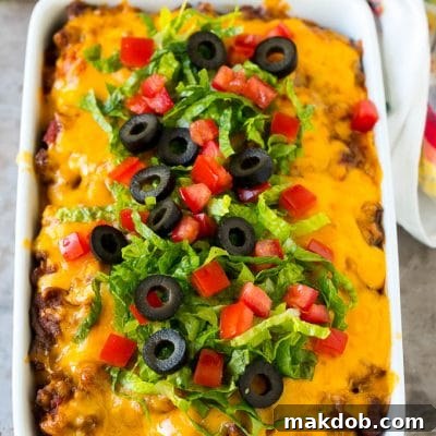 Taco casserole in a baking dish topped with melted cheese, lettuce, tomato and olives.
