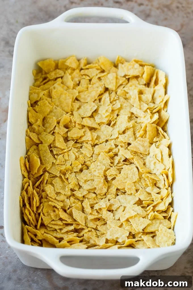 Coarsely crushed golden tortilla chips evenly spread in the bottom of a casserole dish, ready for the next layer.