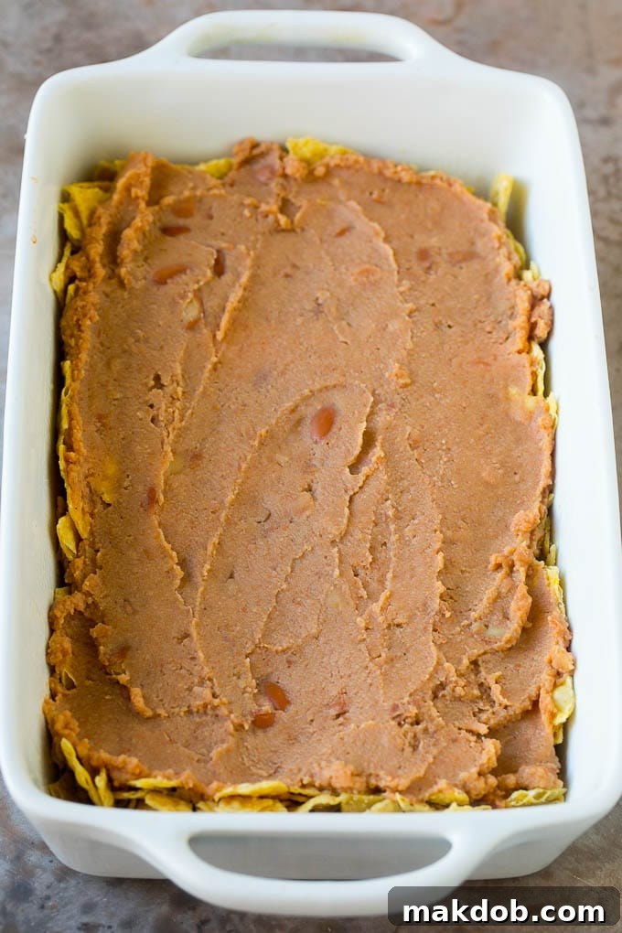 A creamy, smooth layer of refried beans spread over a base of crushed tortilla chips in a baking dish.