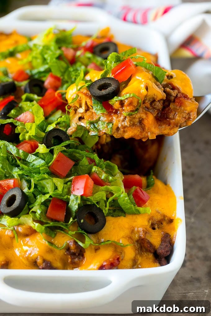 A serving spoon lifting a portion of hot, cheesy beef taco casserole from a baking dish, showcasing the layered ingredients.