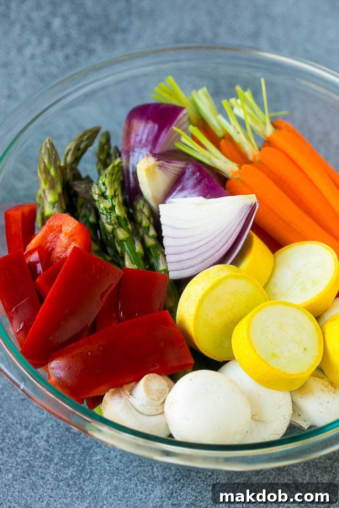 Carrots, bell peppers, yellow squash, mushrooms, and asparagus in a mixing bowl, thoroughly coated with a garlic and herb marinade, ready for grilling.