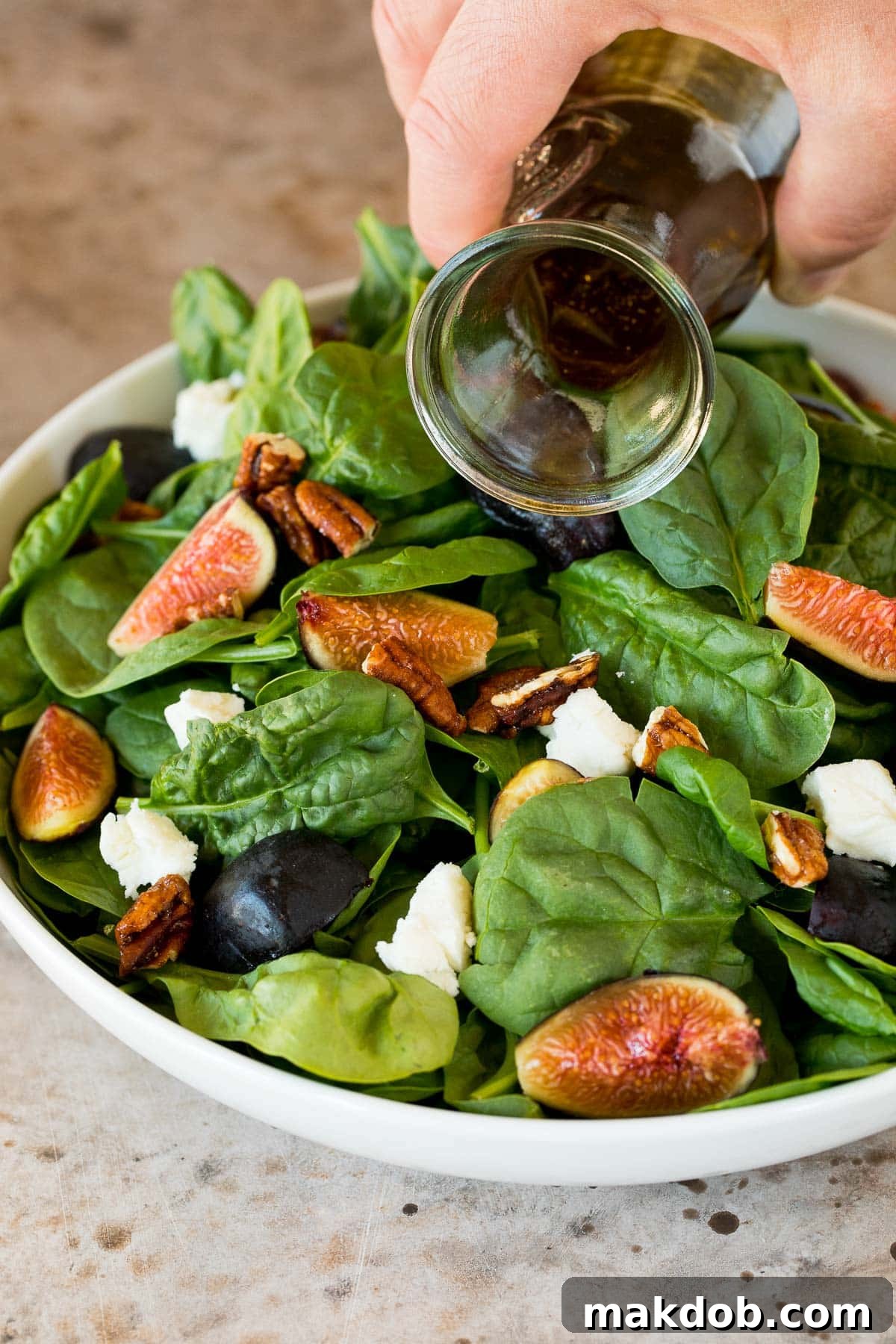 Homemade balsamic vinaigrette being generously drizzled over a fresh fig and spinach salad, creating a luscious coating.