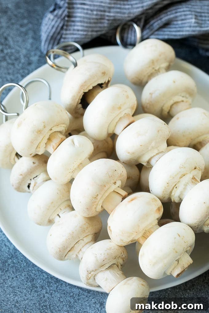 Grilled Mushrooms Recipe | Mushroom Kabobs | Mushroom Side Dish #mushroom #grilling #garlic #keto #lowcarb #dinneratthezoo Fresh button mushrooms threaded onto wooden skewers, ready for grilling.