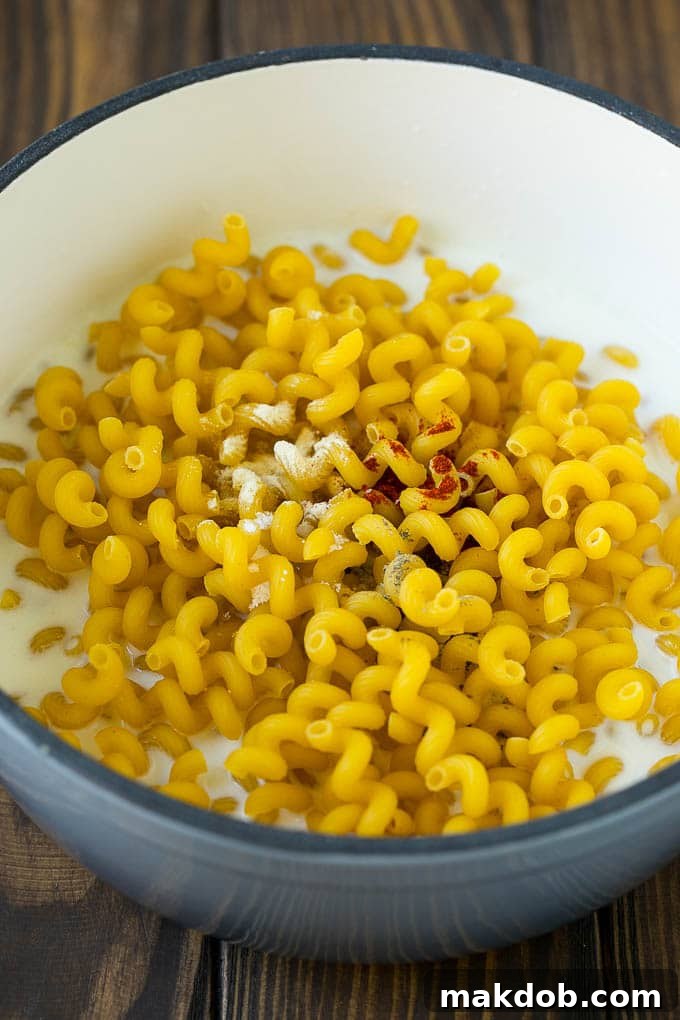 Pasta with milk and spices simmering in a pot, forming the creamy base for mac and cheese.