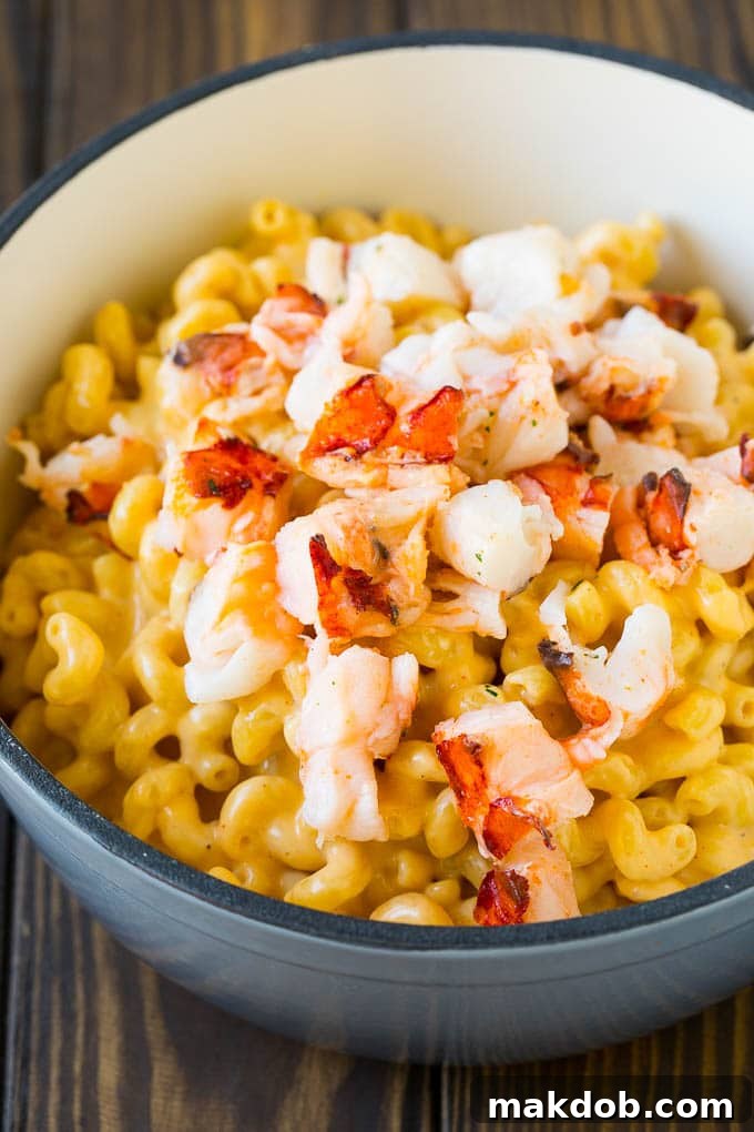 Stove top mac and cheese topped with pieces of cooked lobster, garnished with fresh herbs in a large pot.