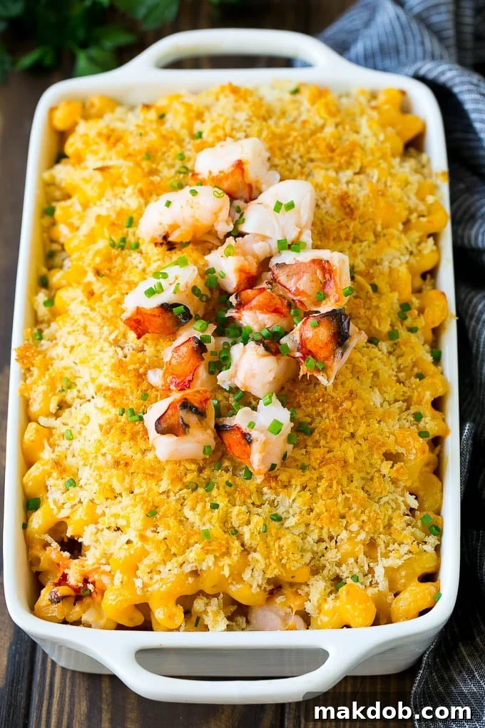 A baking dish of creamy lobster macaroni and cheese, garnished with fresh chives and extra chopped lobster meat.