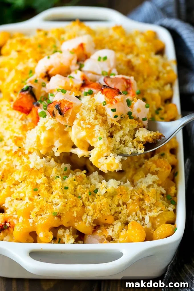 A spoon serving up a portion of rich and creamy lobster mac and cheese from a large dish.