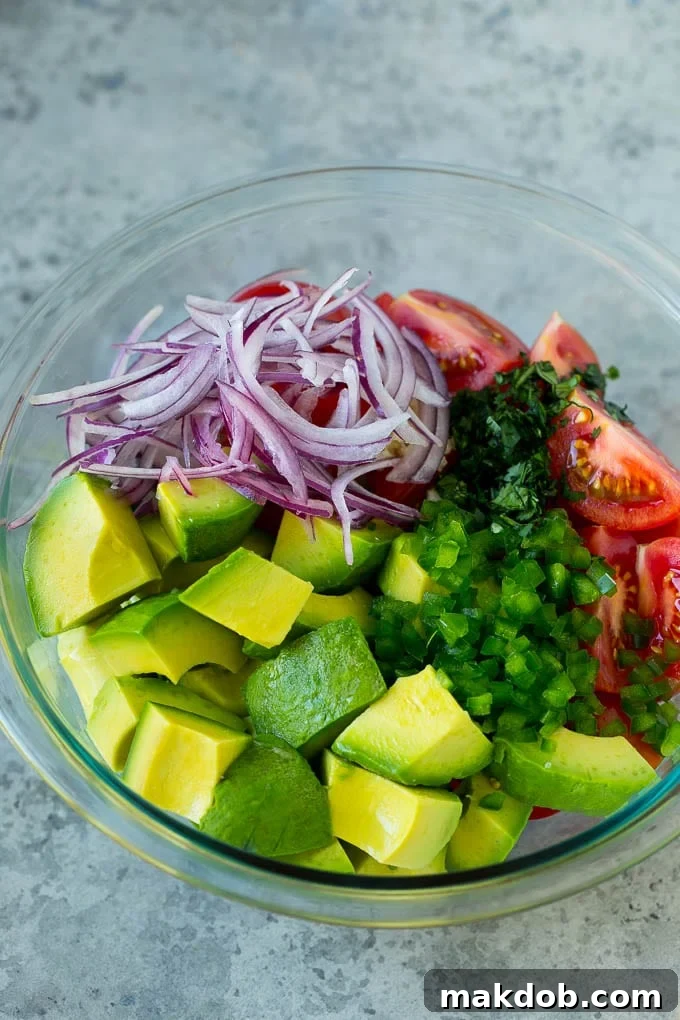Simple Tomato Avocado Salad Ingredients | Fresh Prep | Healthy Recipe Components Close-up of freshly diced avocado, ripe tomato chunks, thinly sliced red onion, and minced jalapeño in a large salad bowl, waiting to be dressed.