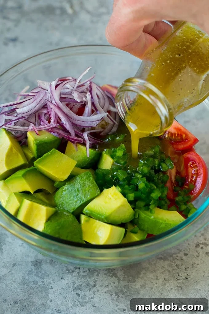 Homemade Lime Dressing for Avocado Salad | Fresh Ingredients | Easy Salad Prep A stream of vibrant lime dressing being poured over a bowl of freshly chopped tomatoes, avocados, and red onions, enhancing their colors.