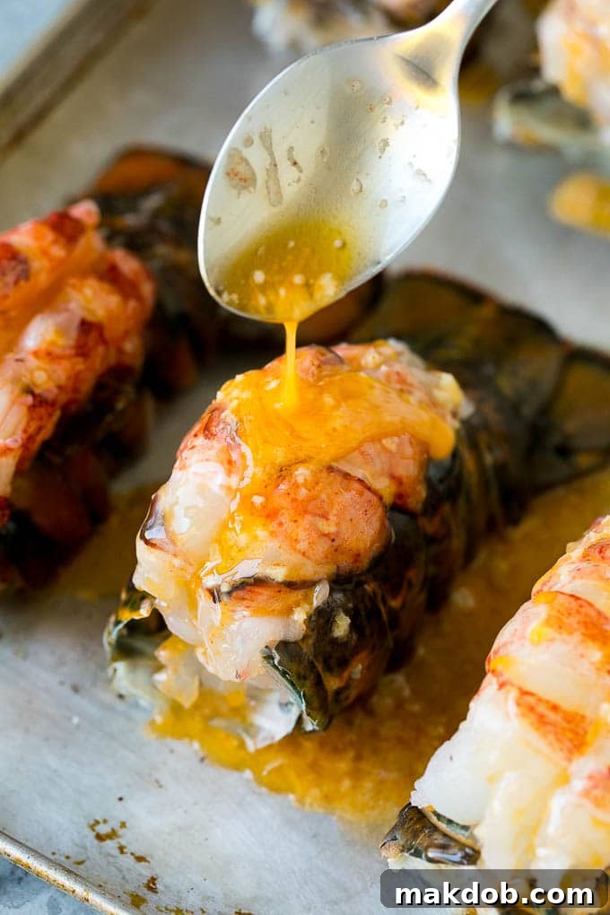 A spoon pouring melted garlic butter over a freshly broiled lobster tail.
