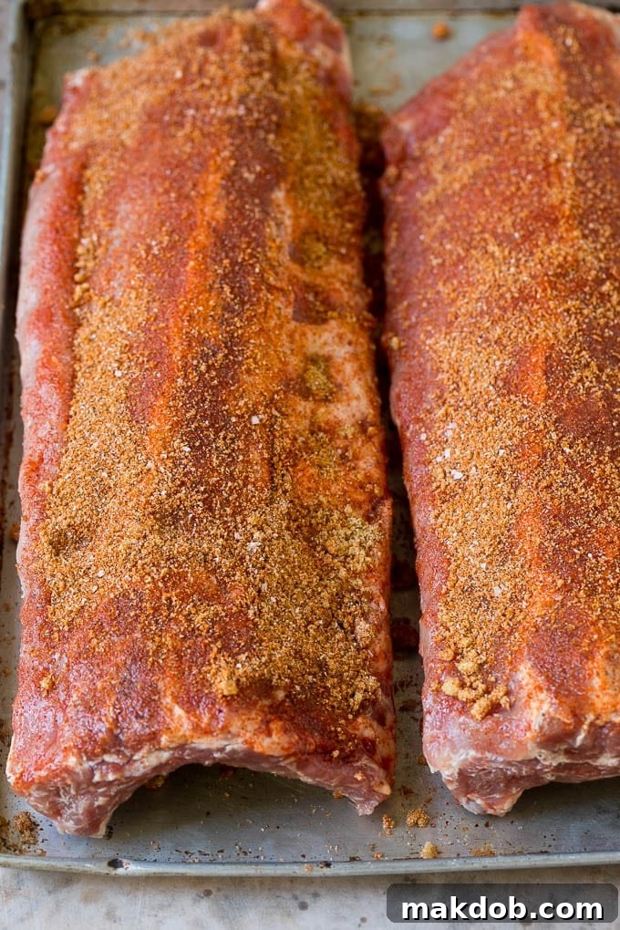 Two racks of baby back ribs generously coated in homemade spice rub, ready for the smoker.