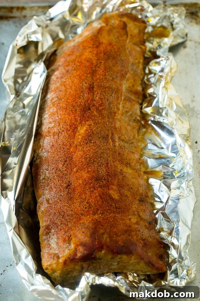 A rack of smoked ribs wrapped tightly in aluminum foil, braising in the smoker.