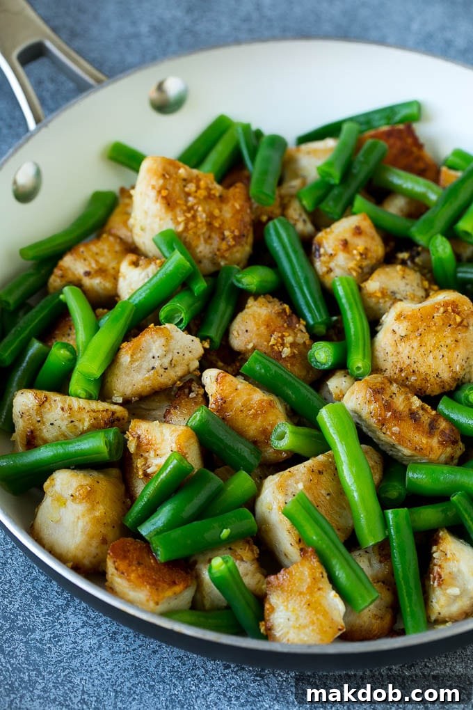 Cooked chicken pieces mixed with vibrant green beans, coated in a glistening honey garlic sauce in a pan.