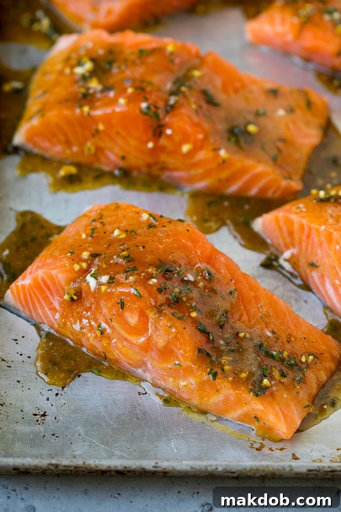 Raw salmon fillets generously coated in a mixture of melted butter, minced garlic, and fresh herbs, ready for baking.