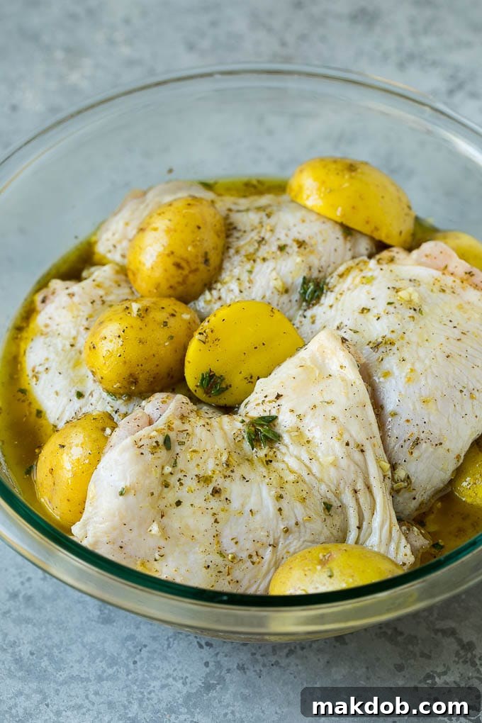 Chicken thighs and potatoes in a garlic and herb marinade, ready for roasting.