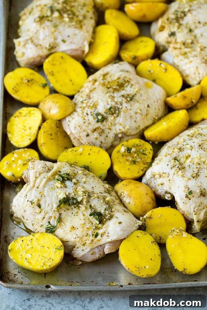 Chicken thighs and potatoes spread out on a sheet pan, ready for the oven.